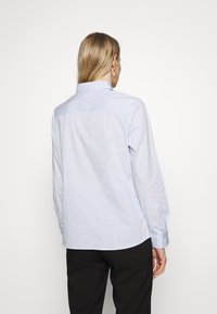 Camicia a righe blu chiaro con colletto abbottonato, maniche lunghe e design con yoke. Realizzata in un tessuto liscio con una consistenza morbida.