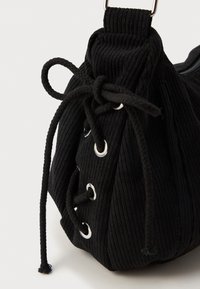 Borsa in tessuto nero con texture a coste, dotata di occhielli in argento e chiusura a coulisse, forma rotonda e design morbido e strutturato.