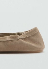 Bailarina de gamuza beige con un exterior suave, puntera redondeada y suela de goma lisa. Detalle de costura a lo largo del borde.