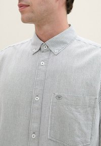 Camisa de botones con un patrón de rayas estrechas en gris y blanco, que presenta un cuello, un bolsillo frontal y botones estándar. Material de algodón.