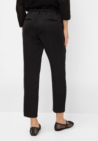 Zwarte broek met een gladde structuur, taps toelopende pijpen en een elastische tailleband. Heeft twee achterzakken en een slank ontwerp.
