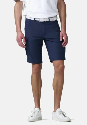 Man draagt marineblauwe cargoshorts met zijzakken, een witte riem, een wit T-shirt en witte sneakers, staand tegen een effen achtergrond.