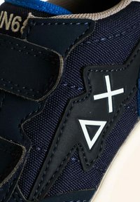 Sneaker blu navy con cinturini in velcro, tomaia in tessuto testurizzato, dettagli sintetici e elementi di design geometrico bianchi.