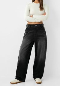 Svarta jeans med vida ben och en blekt design, med hög midja, framfickor och metallknap stängning. Kombinerat med vita sneakers.