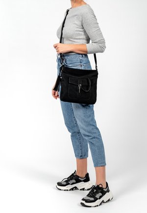 Zwarte suède crossbodytas met een voorvak met klep, zilverkleurige hardware en een tassel-detail. Compacte vorm, ideaal voor dagelijks gebruik of reizen.