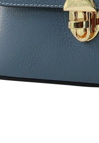 Blauwe leren handtas met een gestructureerde afwerking, voorzien van een goudkleurige sluiting en gestikte details langs de bovenrand. Zwarte bodem.