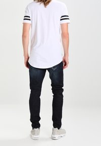 Bílý tričko s černými pruhy na rukávech, spárováno s tmavě modrými džíny a světle šedými teniskami. Důraz na pohodlný střih a materiály.