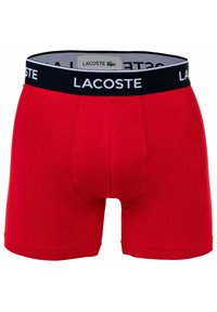 Czerwone bawełniane męskie bokserki z czarnym paskiem w talii, na którym w białym kolorze widnieje napis "LACOSTE". Dopasowany krój i gładka tekstura.