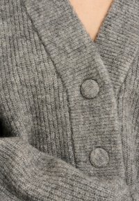 Grau Strickjacke mit V-Ausschnitt, gerippter Textur und zwei runden Knöpfen. Weiches Wollmaterial zeigt subtile Variationen in Farbton und Muster.