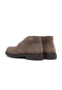Botas de hombre de ante marrón hasta el tobillo con suelas de goma oscuras, costuras visibles y diseño de puntera redonda sobre un fondo blanco.