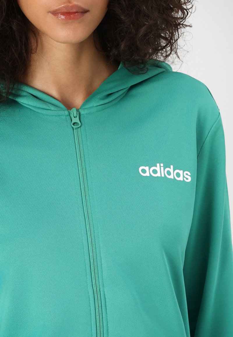 Felpa con zip di colore verde acqua realizzata in tessuto morbido, dotata di cappuccio con cordino e logo "adidas" bianco nella parte sinistra del petto.