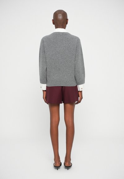 Grauer Strickpullover mit V-Ausschnitt, langen Ärmeln und weißem Kragen, kombiniert mit kastanienbraunen Shorts. Weiche Textur und lässiges Design.