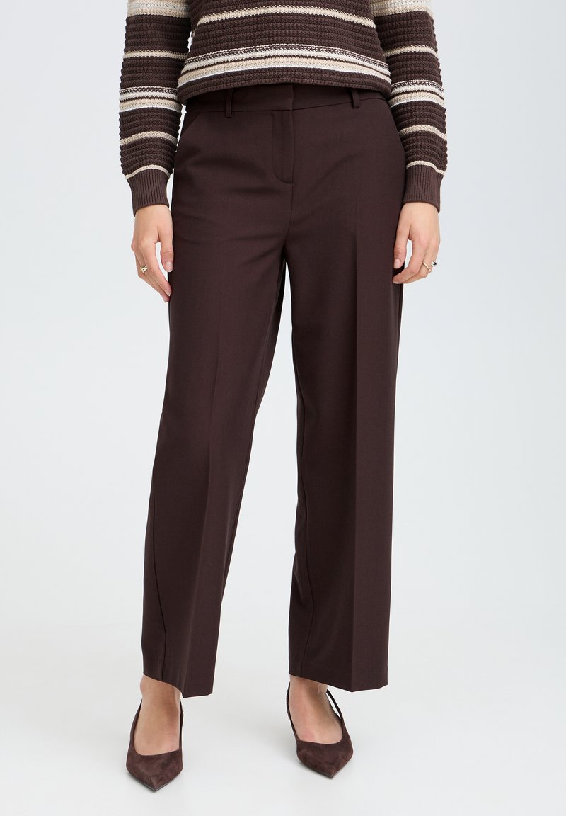 Femme portant un pantalon droit marron foncé associé à un pull en tricot rayé marron et des chaussures pointues marron foncé.
