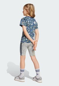 Tričko s kvetinovou potlačou a krátkymi rukávmi, modrá základná farba. Šortky so vzorom s krémovými a modrými akcentmi. Šedé tenisky s bielymi pruhmi.