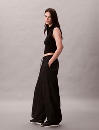 Μαύρο αμάνικο cropped top συνδυασμένο με χαλαρές μαύρες παντελόνες που διαθέτουν πλαϊνές τσέπες και ελαστική μέση, συμπληρωμένο με μαύρα sneakers.