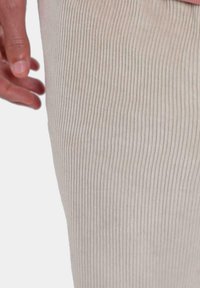 Primer plano de una tela beige acanalada con líneas verticales, textura suave y una mano descansando en un lado, resaltando el detalle de la tela.