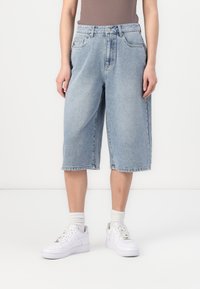 Culottes de denim azul claro con un corte relajado, cintura media y diseño de cinco bolsillos. Llevados con zapatillas blancas y calcetas acanaladas.
