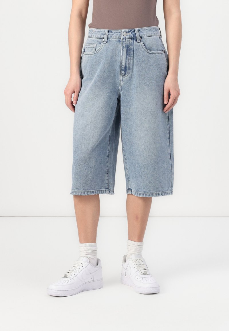 Culottes de denim azul claro con un corte relajado, cintura media y diseño de cinco bolsillos. Llevados con zapatillas blancas y calcetas acanaladas.