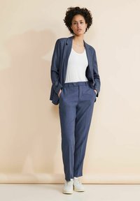 Suit blu su misura con vestibilità comoda, caratterizzato da un blazer a un bottone e pantaloni dritti, abbinato a una canotta bianca e sneakers bianche.