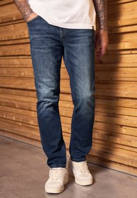 Mörkblå denimjeans med slim fit, med subtila blekningar, standardfickor och kompletterat med ljusa sneakers.