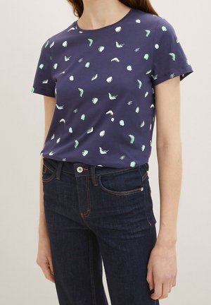 Marineblaues kurzärmeliges T-Shirt aus Baumwolle mit einem Muster aus grünen und weißen Formen, kombiniert mit dunklen Jeans aus Denim.