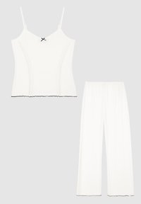 Camiseta blanca sin mangas con tirantes finos y un detalle de lazo negro en el centro, combinada con pantalones blancos de pierna ancha. Ambos tienen bordes festoneados.