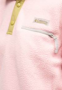 Φλις πουλόβερ σε απαλό ροζ με γιακά σε χρώμα καφέ και κουμπιά, με τσέπη με φερμουάρ σε γκρι και λογότυπο Columbia στο στήθος.