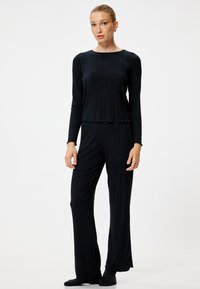 Donkere, geribbelde lounge-set met een aansluitend longsleeve top en wijde broek. De stof heeft een zachte textuur en een subtiele glans.