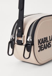 Borsa in ecopelle beige con hardware nero, doppi zip e branding "KARLA JEANS" in nero. Presenta una forma compatta e arrotondata con una finitura texturizzata.