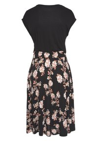 Haut noir à manches courtes associé à une jupe midi noire avec imprimé floral pêche et blanc, vue de dos.