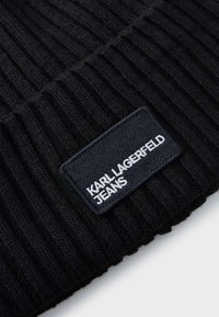 Čierna rebrovaná pletenina s obdĺžnikovou čiernou nášivkou, na ktorej je v bielych veľkých písmenách napísané "KARL LAGERFELD JEANS".