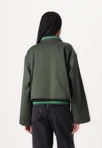 Groene croppeddonker met kraag, brede mouwen en een groen gestreepte zoom. Gladde stof, minimalistisch ontwerp en geen zichtbare sluitingen.