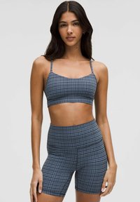 Conjunto deportivo de cuadros azules que presenta un top corto con tirantes finos y pantalones cortos de cintura alta, fabricado en un tejido liso y elástico.