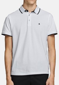Witte polo met een zwarte kraag en manchetten. Beschikt over een drieknoopsluiting en een klein logo op de linkerborst. Soepele stofstructuur.