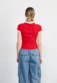 Red short-sleeve fitted t-shirt with white ribbed neckline, paired with light blue baggy cargo pants featuring side pockets and buttoned flaps.