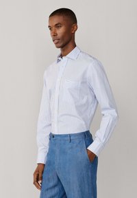 Chemise à manches longues rayée bleu clair et blanc, en coton avec une poche, associée à un pantalon bleu clair, avec une fermeture à boutons.