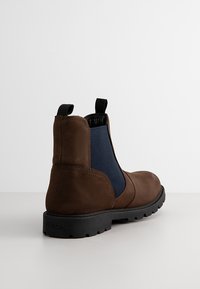 Stivaletto in pelle marrone con pannelli elastici laterali blu e suola in gomma nera. Presenta un'apposita linguetta sul retro e una finitura texturizzata.