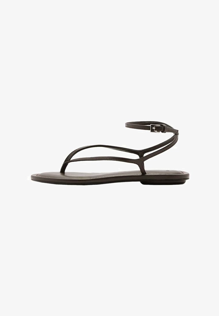Sandale plate noire avec fines lanières, fermeture à boucle à la cheville, et un design minimaliste vue de profil sur un fond blanc.
