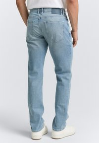 Lichtblauwe spijkerbroeken met een rechte snit, vijf zakken en een leren label op de achterkant van de taille. Witte sneakers complementeren de outfit.