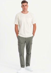 Cremefarvet t-shirt med korte ærmer og brystlomme, parret med olivengrønne cargobukser med sidelommer, suppleret med hvide sneakers.