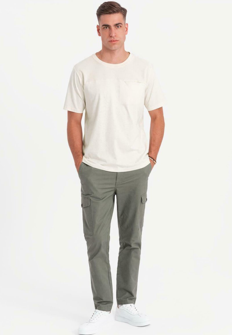 Cremefarvet t-shirt med korte ærmer og brystlomme, parret med olivengrønne cargobukser med sidelommer, suppleret med hvide sneakers.