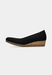 Chaussure noire à semelle compensée basse avec bout rond et semelle intermédiaire texturée liège sur une semelle en caoutchouc beige sur fond uni.
