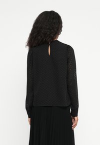 Black blouse with long sleeves, textured zigzag pattern, back keyhole detail, and soft, lightweight fabric.