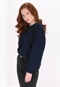 Maglietta a maniche lunghe blu navy con vestibilità comoda e maniche a sbuffo, abbinata a jeans in denim neri a vita alta, presentata su uno sfondo neutro.