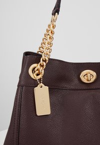 Bordowa skórzana torebka o teksturowanym wykończeniu, z paskiem na łańcuszku w złotym kolorze i metalowymi okuciami. Posiada złotą metkę z nazwą marki.