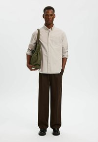 Φωτεινό μπεζ πουκάμισο με κουμπιά και τσέπη στο στήθος, συνδυασμένο με καφέ παντελόνια φαρδιάς γραμμής και μαύρα παπούτσια. Πράσινη τσάντα με σχεδιασμό συγκέντρωσης.