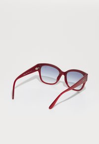 Ochelari de soare roșii din acetat, cu lentile cu nuanță gradient, rame late și brațe elegante, prezentând detalii din metal argintiu.