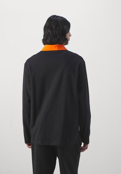 Svart langermet skjorte med oransje krage, laget av bomull. Enkel design med en avslappet passform, sett fra baksiden.