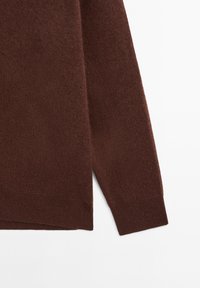Brun stickad tröja med en mjuk textur, långa ärmar och sidoflikar. Tyget verkar lätt och har en något luddig yta.