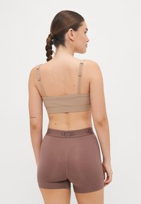 Smeđi rebrasti bralet i odgovarajući smeđi bokserice s UGG logom na pojasu, bez šavova i glatke teksture.